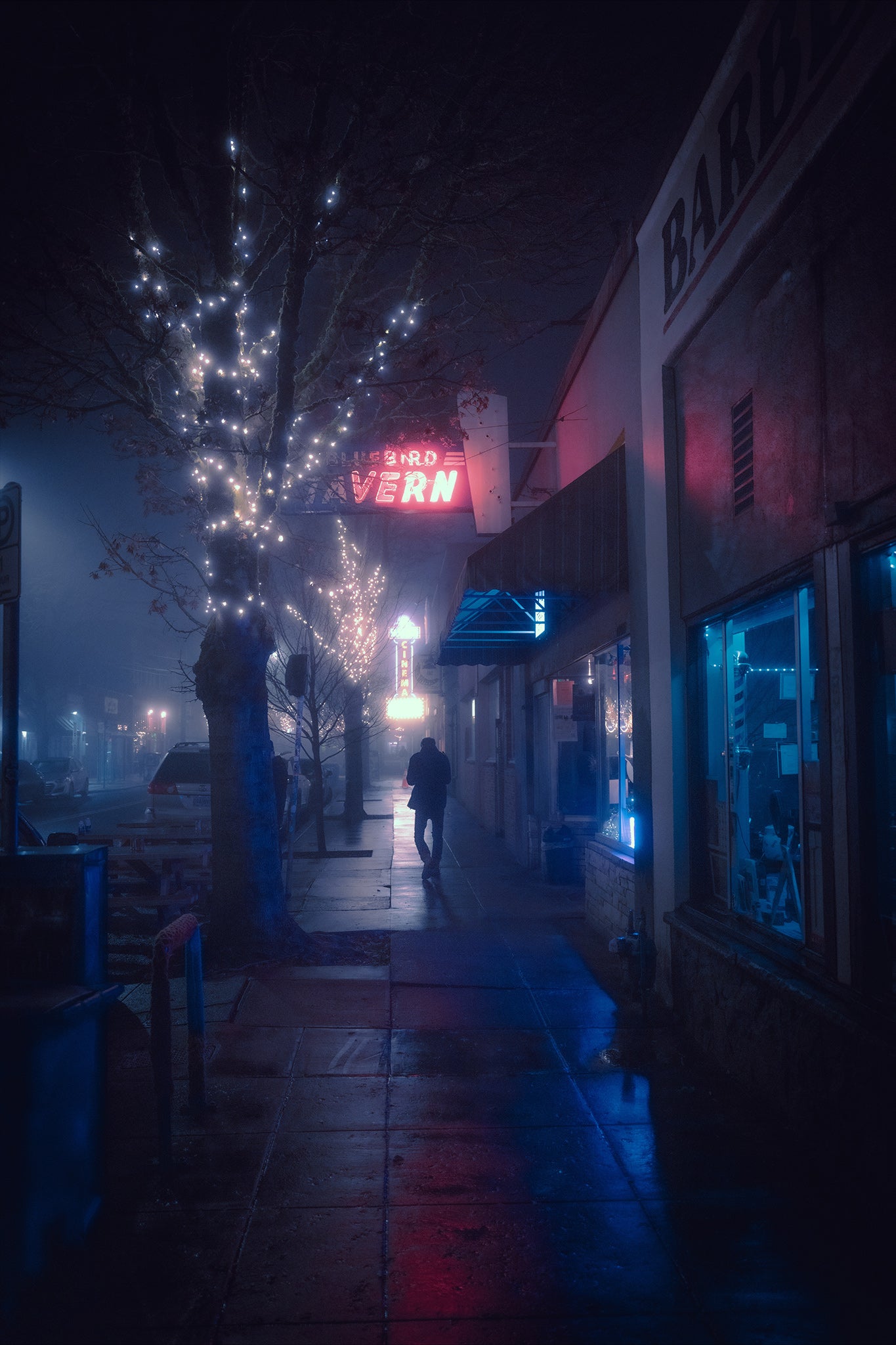 A man walking alone in an empty street on a foggy night.