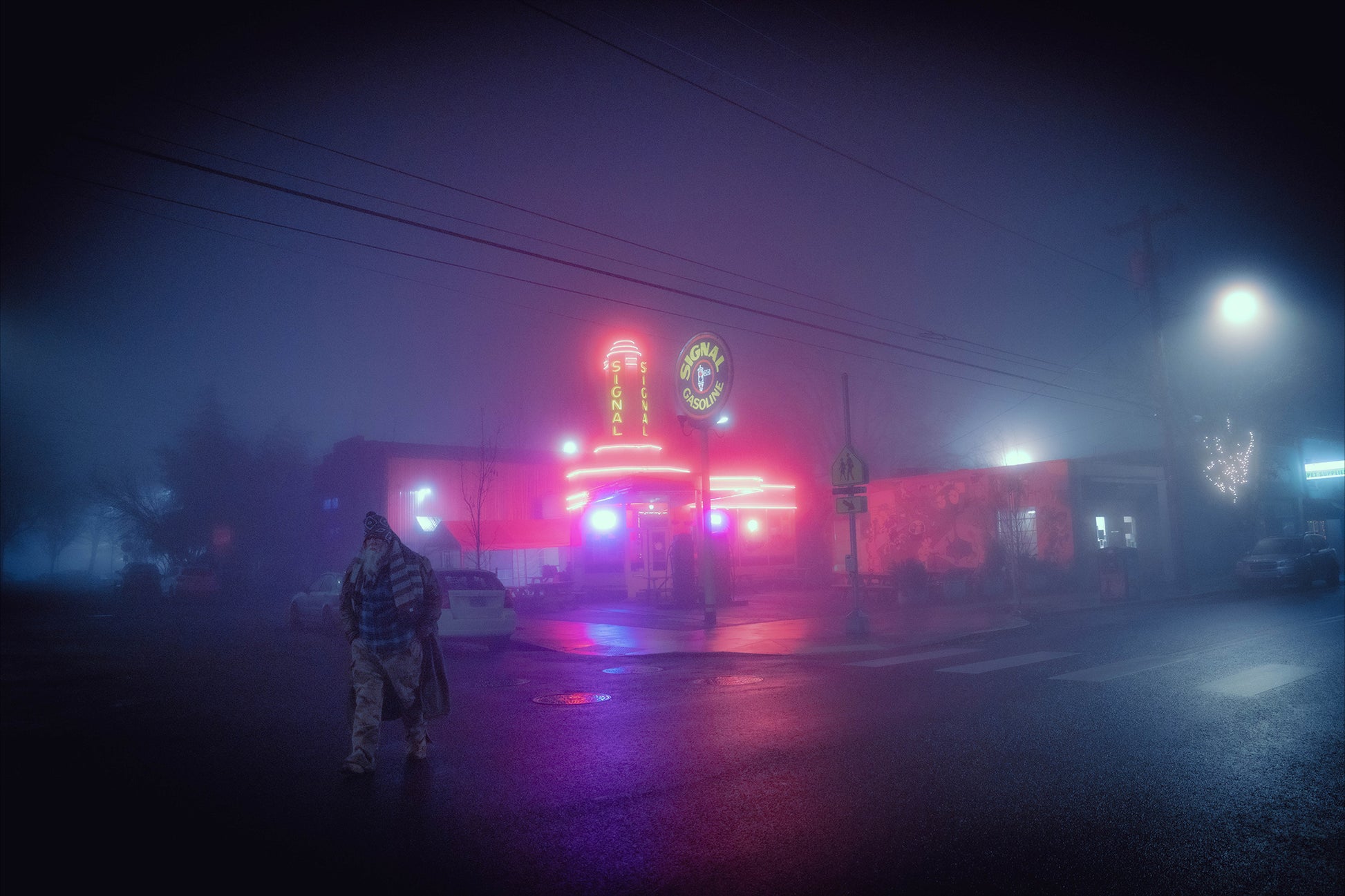 a man walking away from a gas station with neon lights on a very foggy night