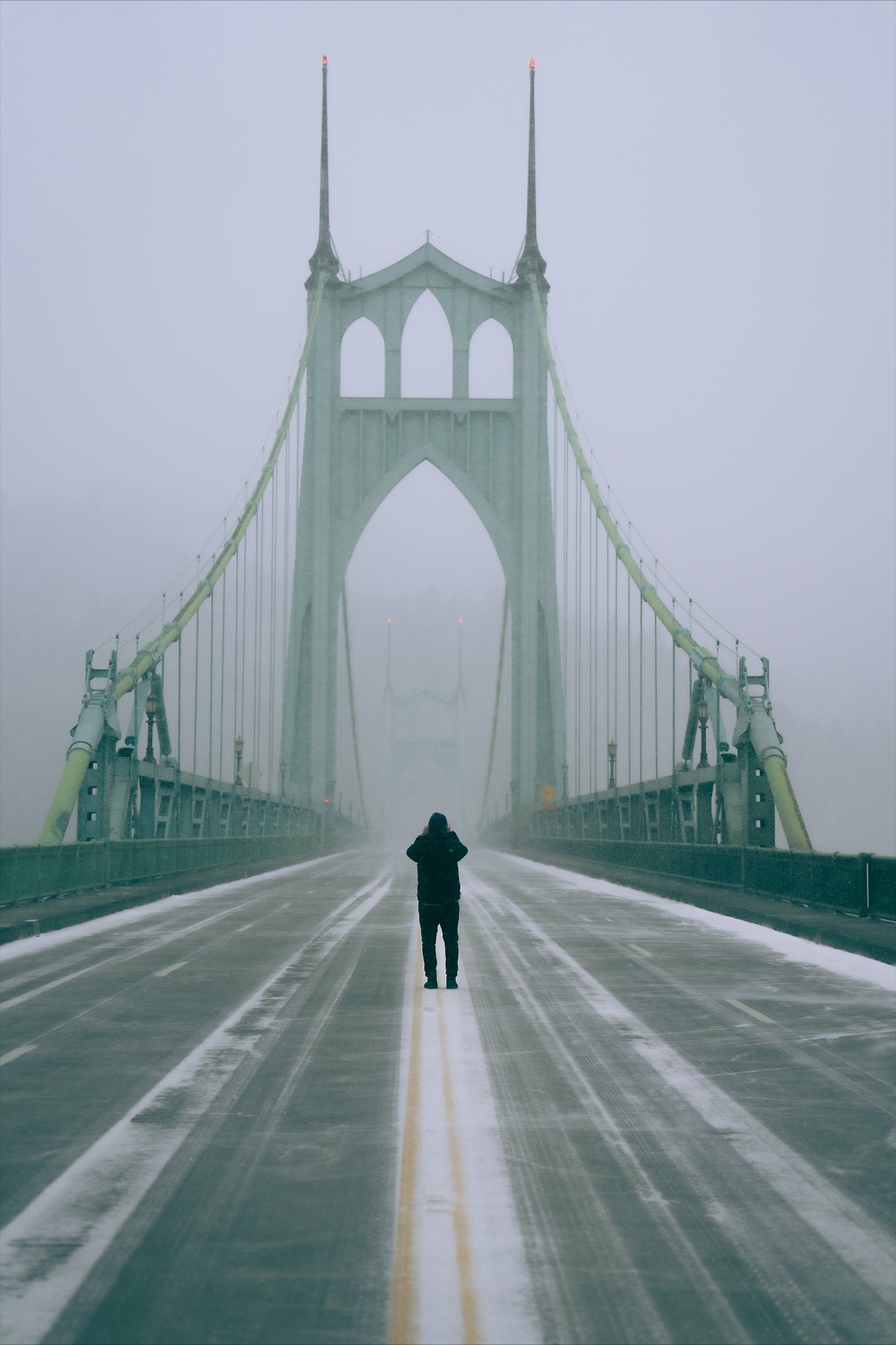 a man in the middle of the road on the st johns bridge taking a picture during a snowstorm