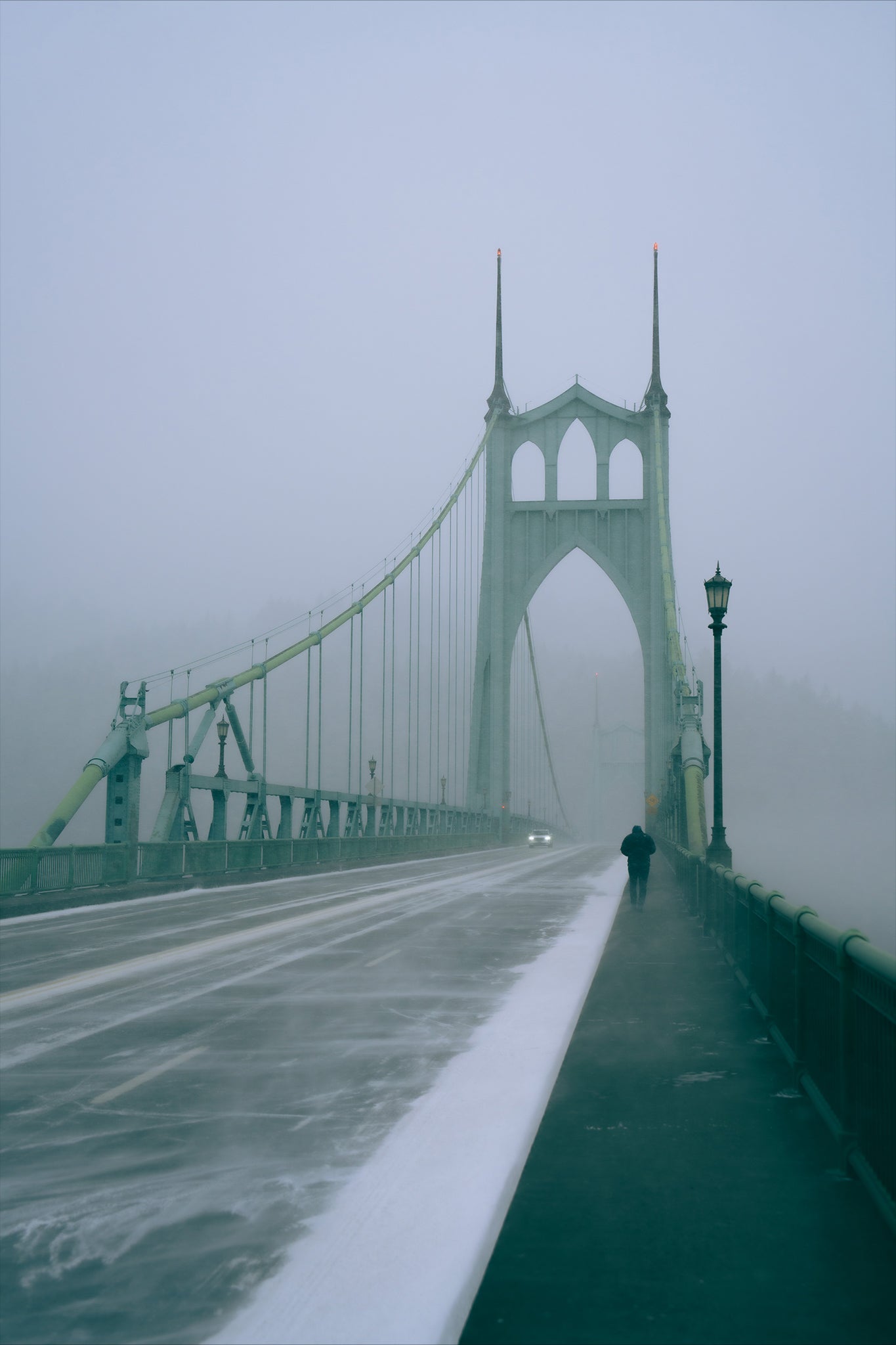 a man walking across the st johns bridge during a snowstorm in portland